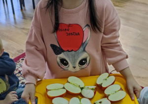 Dziewczynka stoi z tacą przekrojonych jabłek